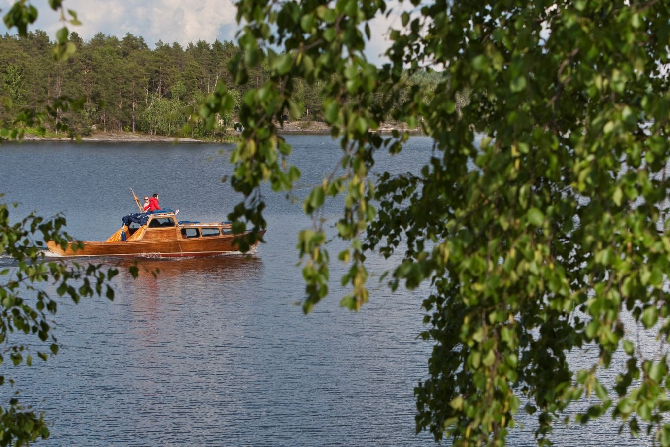 Puinen vene järvellä kuvattuna koivun oksien takaa.